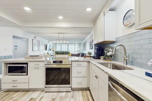 A modern kitchen with white cabinetry, a built-in oven, a microwave, and a stainless steel sink. - Beachfront Shoreline Towers condo on 2nd floor only steps away from beach (Destin)