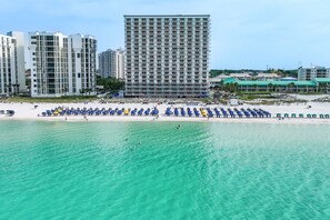 A beach with rows of umbrellas and a tall building in the background. - Beachfront with a heated pool & a spa (Destin)