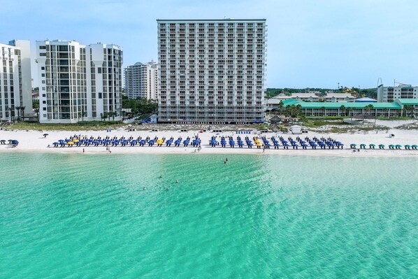 Ein Strand mit Reihen von Sonnenschirmen und einem hohen Gebäude im Hintergrund.