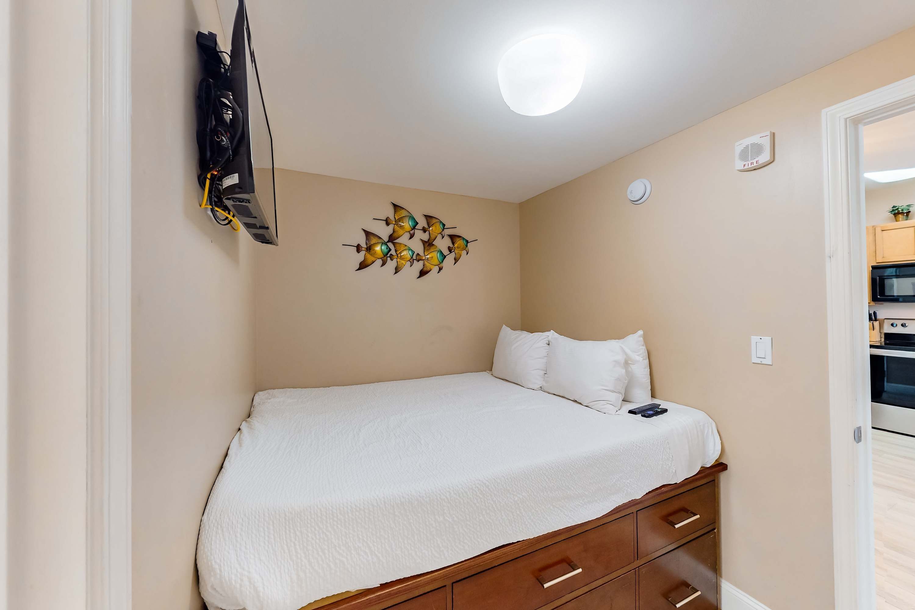 Een slaapkamer met een bed, een tv aan de muur, een plafondlamp en decoratieve viskunst aan de muur.