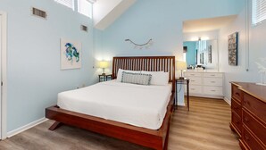 Ein Schlafzimmer mit einem hölzernen Bett, weißer Bettwäsche, einem Nachttisch, einem Schminktisch und einem Spiegel.