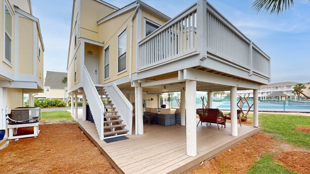 Ein zweistöckiges Haus mit überdachter Terrasse, einer Treppe und Sitzgelegenheiten im Freien.
