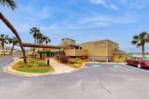A hotel with a covered entrance, palm trees, and a parking lot with blue handicapped parking spaces. - Snowbird & dog-friendly condo with 5 pools, hot tubs, golf, tennis, pickleball (Destin)