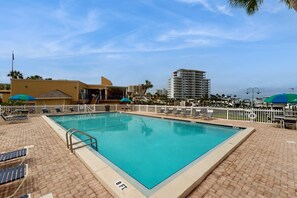 A rectangular swimming pool with a tiled deck, surrounded by lounge chairs and umbrellas. - Snowbird & dog-friendly condo with 5 pools, hot tubs, golf, tennis, pickleball (Destin)