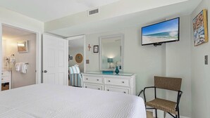 A bedroom with a large bed, a television mounted on the wall, a dresser, a chair, and a door leading to another room. - Coastal condo with Gulf views, washer and dryer, Wifi, Community pool (Destin)