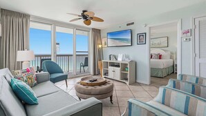 A hotel room with a balcony, a sofa, a chair, a small ottoman, a TV, and a bed. - Coastal condo with Gulf views, washer and dryer, Wifi, Community pool (Destin)