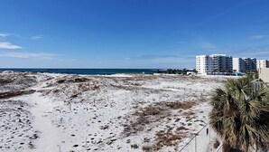 A beach with sandy terrain, a clear blue sky, and a few buildings in the background. - Beachfront Condo, gorgeous views, beach access & close to everything (Destin)