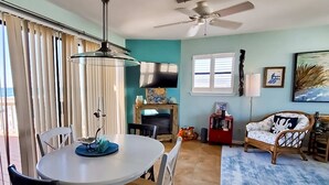 A dining area with a round table, chairs, a ceiling fan, and a television. - Beachfront Condo, gorgeous views, beach access & close to everything (Destin)