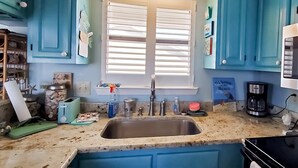 A kitchen with blue cabinets, a sink, a window with blinds, and various kitchen items. - Beachfront Condo, gorgeous views, beach access & close to everything (Destin)