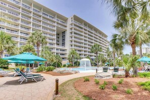 A hotel with multiple floors, outdoor pool area with lounge chairs and umbrellas, and palm trees. - Ocean-View Getaway with Two Shared Pools, Gym & Beach Access (Destin)