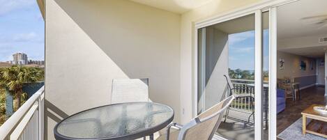 A balcony with a glass table and chairs, a sliding glass door leading to an interior space with a sofa and a coffee table.