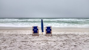 Zwei Strandstühle mit Handtüchern an einem Sandstrand, im Hintergrund das Meer.