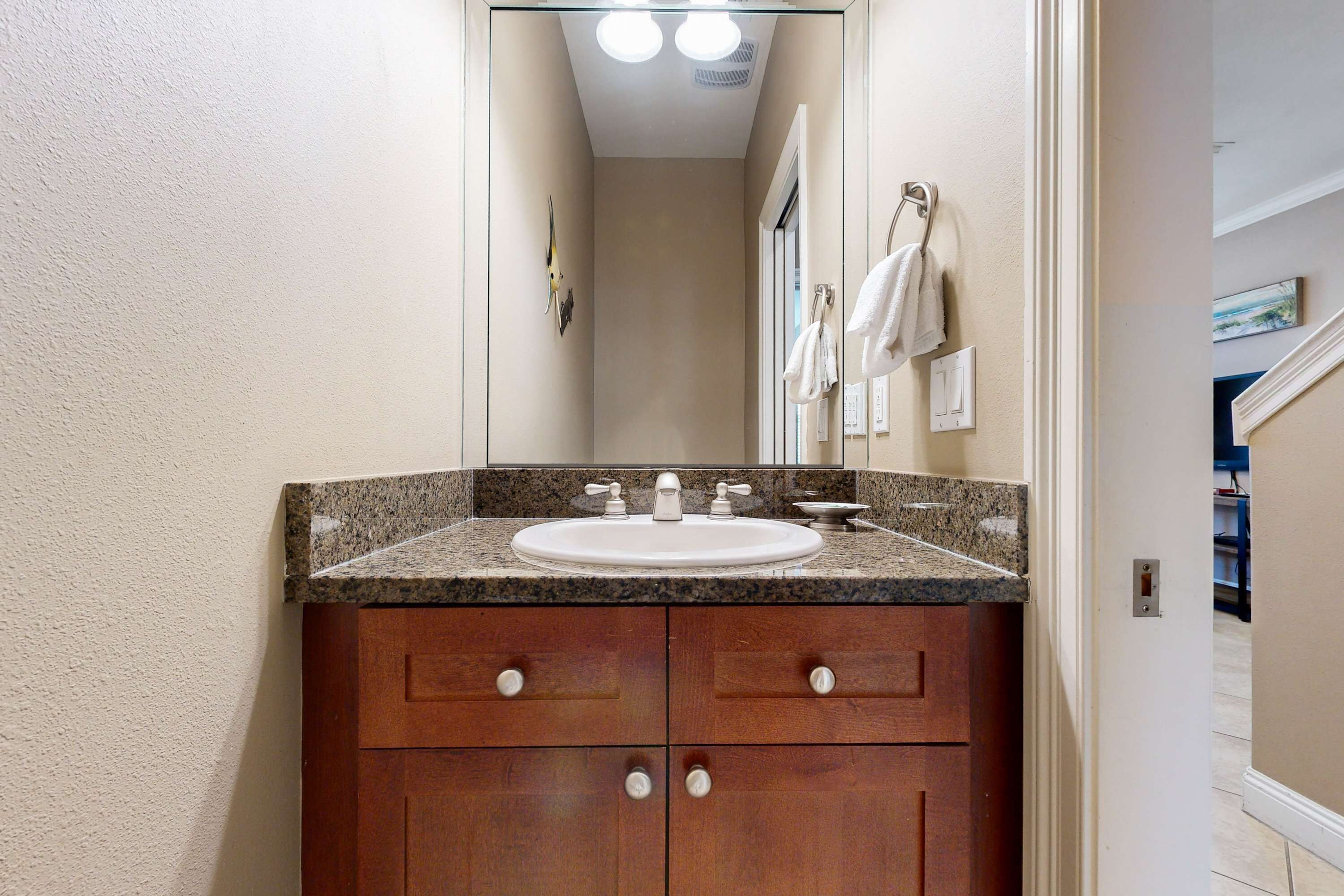 A bathroom with a granite countertop sink, wooden vanity with four drawers, a mirror above the sink, and a towel rack on the wall.