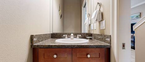 A bathroom with a granite countertop sink, wooden vanity with four drawers, a mirror above the sink, and a towel rack on the wall.