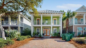 A two-story building with a green and white facade, a covered front porch, and a brick driveway. - Nautical home in gated community with pool, hot tub & beach access (Destin)