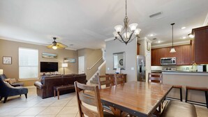 A spacious living room with a large wooden dining table, comfortable seating, and a ceiling fan. - Nautical home in gated community with pool, hot tub & beach access (Destin)