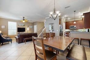 A spacious living room with a large wooden dining table, comfortable seating, and a ceiling fan. - Nautical home in gated community with pool, hot tub & beach access (Destin)