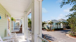 A covered porch with white railings, a green building, and a street view with other buildings and palm trees. - Nautical home in gated community with pool, hot tub & beach access (Destin)