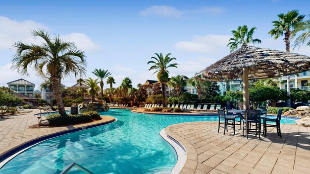 A swimming pool with a curved edge, surrounded by lounge chairs and a thatched umbrella. - Nautical home in gated community with pool, hot tub & beach access (Destin)