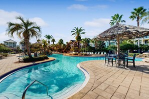 Une piscine à bord incurvé, entourée de chaises longues et d’un parasol en feuilles de palmier.
