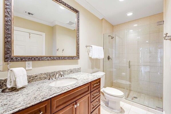 A bathroom with a marble sink, wooden vanity, a large mirror, a glass-enclosed shower, and a toilet. - Penthouse condo Emerald Grande with pools, hot tubs, gym - water view balconies (Destin)