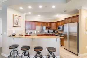 A modern kitchen with a central island, stainless steel appliances, wooden cabinets, and a bar stool seating area. - Penthouse condo Emerald Grande with pools, hot tubs, gym - water view balconies (Destin)