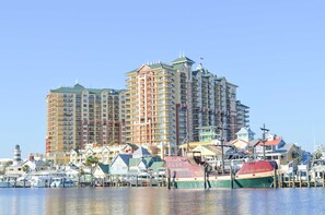 A multi-story hotel with balconies, a marina with boats, and a lighthouse in the background. - Penthouse condo Emerald Grande with pools, hot tubs, gym - water view balconies (Destin)