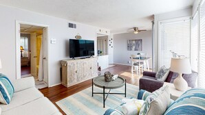 A living room with a sofa, a coffee table, and a TV. There is a dining area with a table and chairs. - Charming condo with pool, hot tub, tennis, balcony, & W&D (Destin)