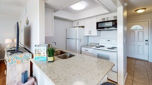 A modern kitchen with white cabinets, a stainless steel microwave, a white refrigerator, and a built-in oven. - Charming condo with pool, hot tub, tennis, balcony, & W&D (Destin)
