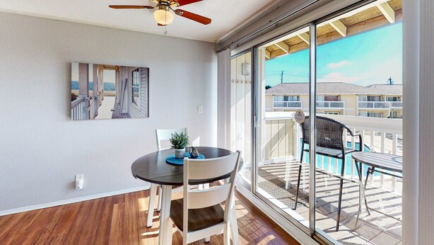 A room with a ceiling fan, a large window, a dining table with chairs, and a painting on the wall. - Charming condo with pool, hot tub, tennis, balcony, & W&D (Destin)