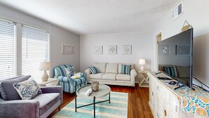 A living room with a sofa, armchair, coffee table, and a sideboard. - Charming condo with pool, hot tub, tennis, balcony, & W&D (Destin)