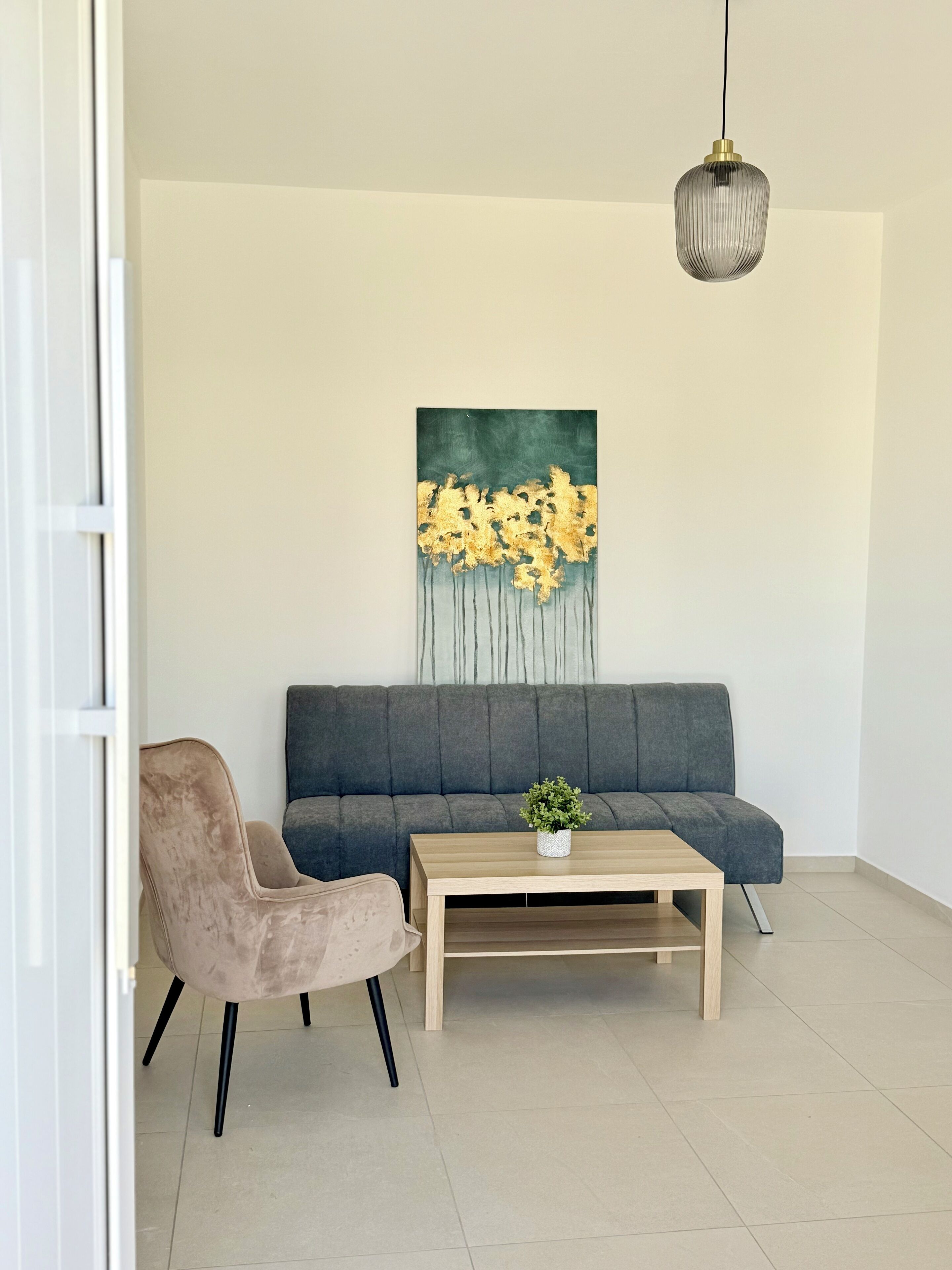 Uma sala de estar moderna com um sofá cinzento, uma poltrona bege e uma mesa de centro de madeira.