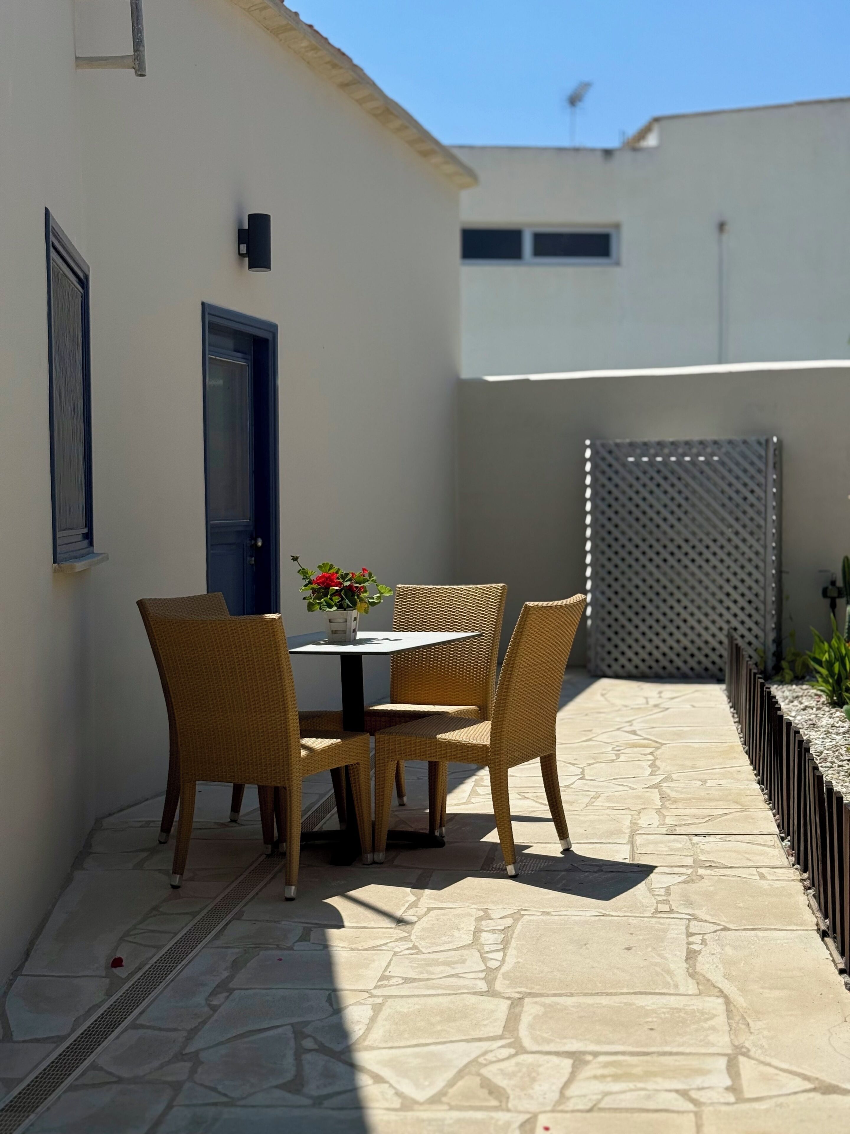 An outdoor patio with a table and chairs, a door, and a wall-mounted light fixture.