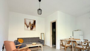 A modern living room with a grey sofa, a peach armchair, and a wooden dining table with four chairs. A painting is on the wall, and a pendant light hangs from the ceiling. - Kiti Traditional Residences (Kiti)
