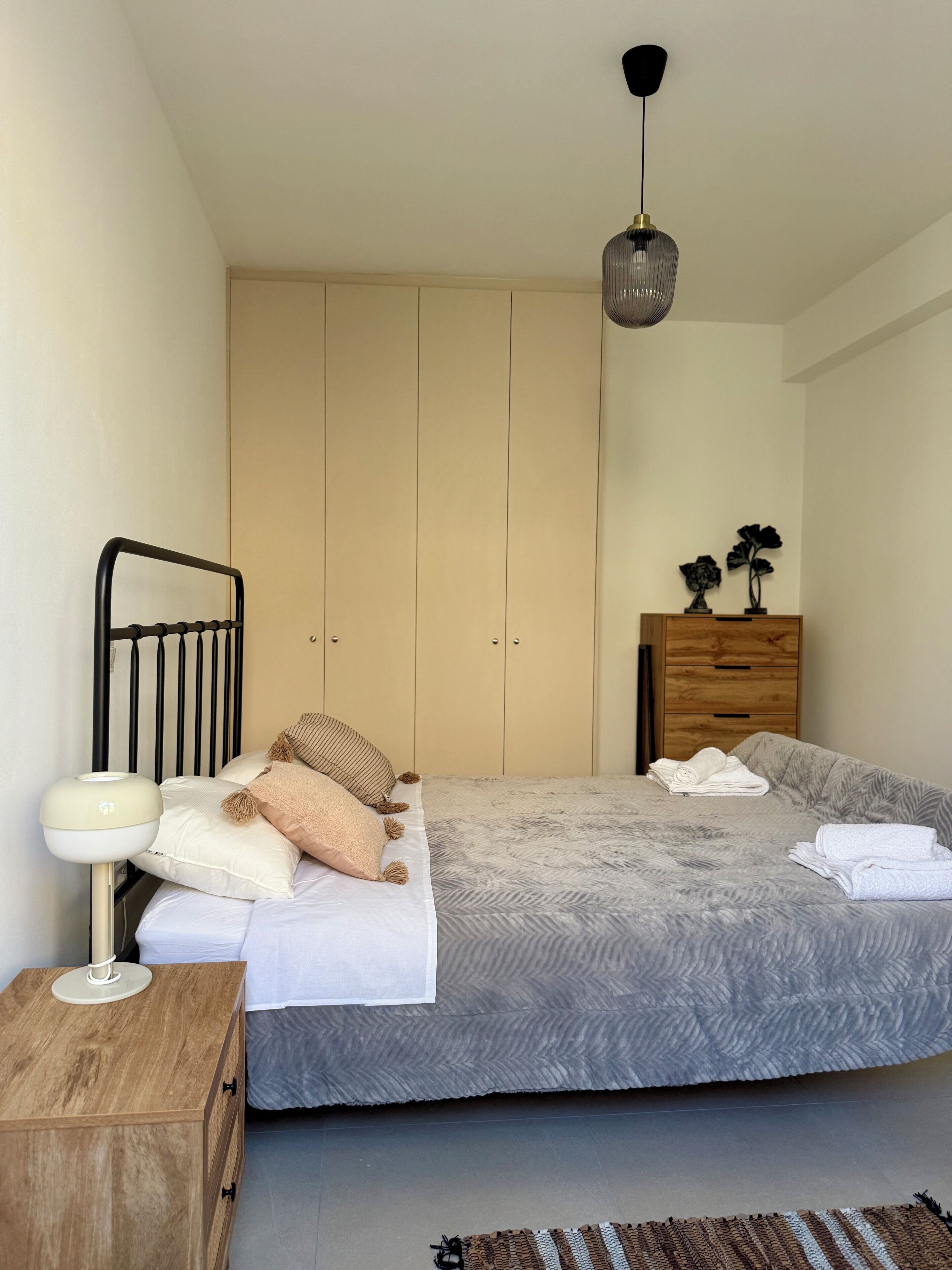 A neatly arranged bedroom with a bed, bedside table, lamp, and a wooden dresser.