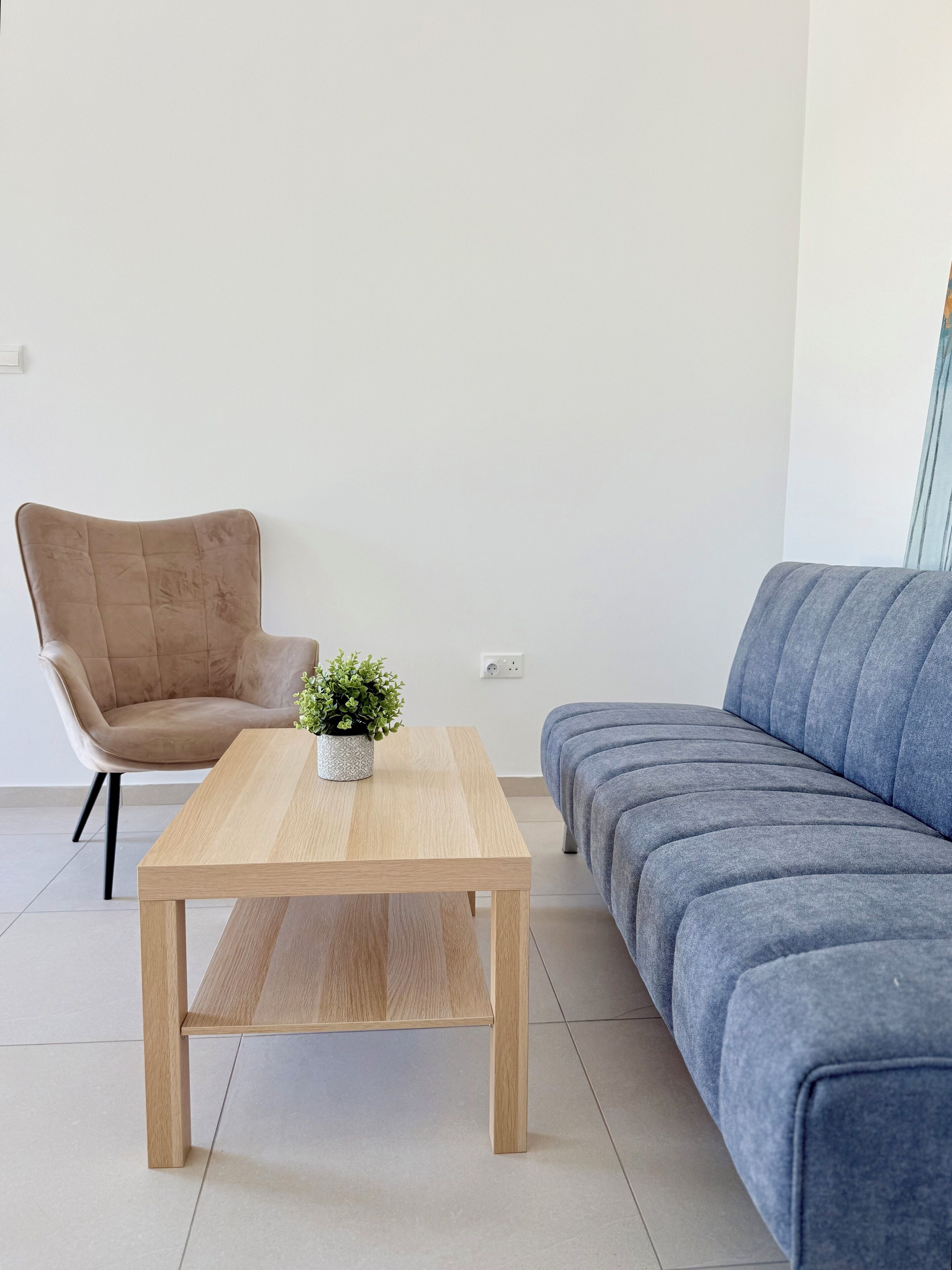 A modern living room with a wooden coffee table, a beige armchair, and a blue sofa.