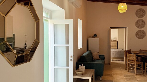 A spacious living area with a wooden ceiling, a large mirror, a green sofa, a dining table, and a kitchen visible through an open door. - Kiti Traditional Residences (Kiti)