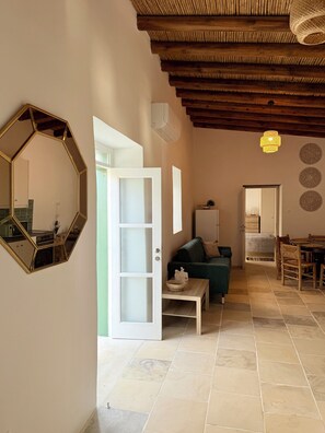 A spacious living area with a wooden ceiling, a large mirror, a green sofa, a dining table, and a kitchen visible through an open door. - Kiti Traditional Residences (Kiti)