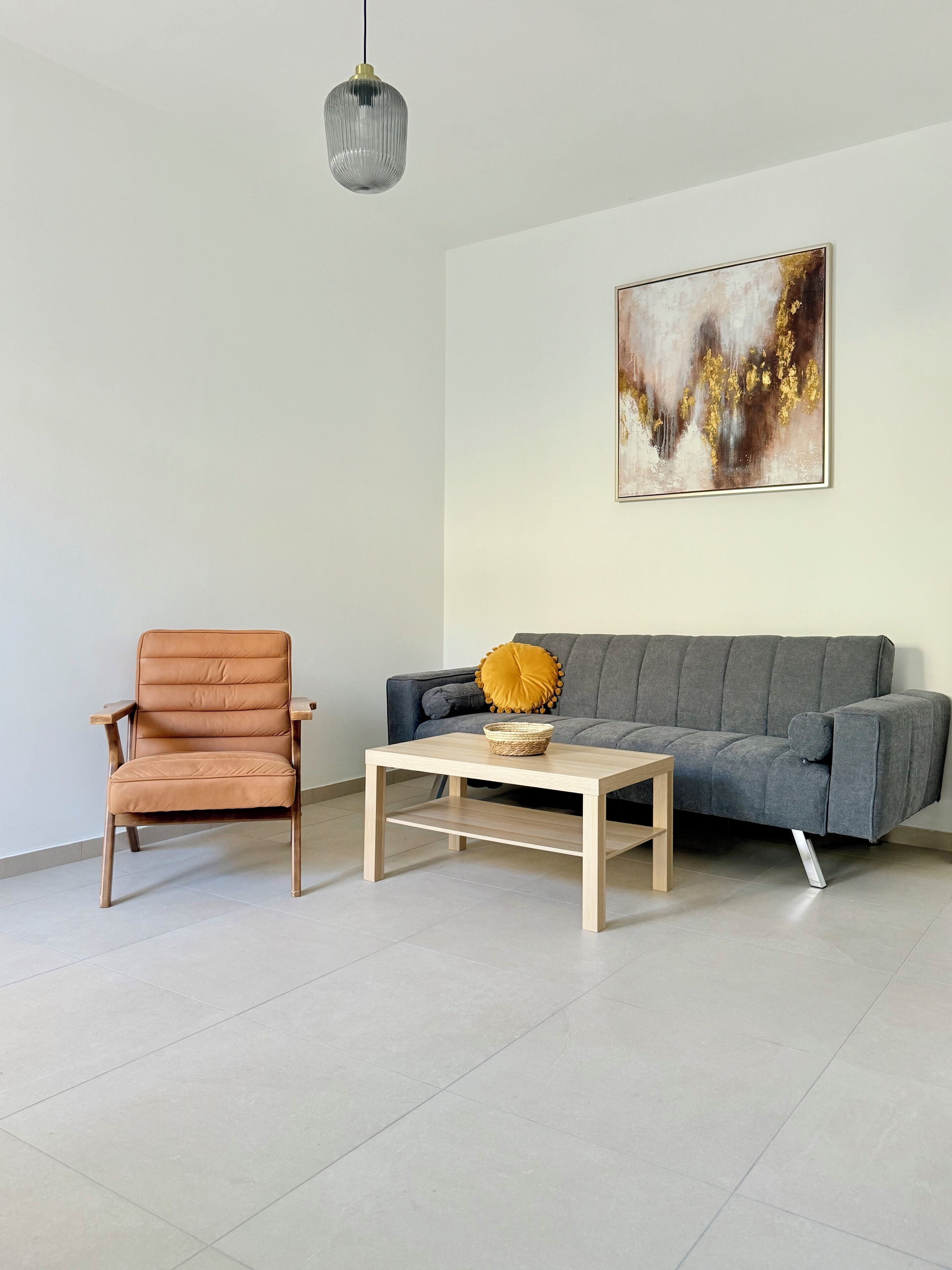 Una sala de estar con un sofá gris, un sillón de cuero marrón, una mesa de centro de madera y una lámpara colgante.