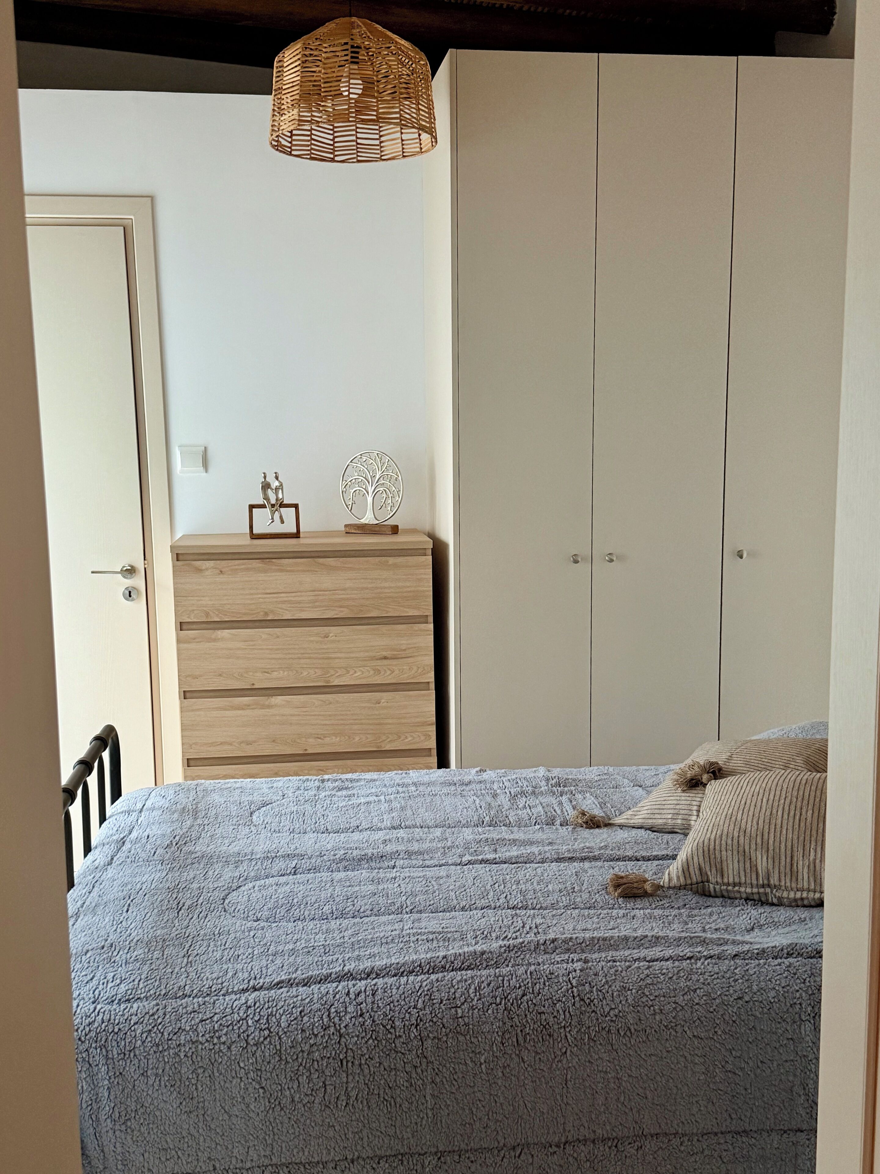 Une chambre à coucher comprenant un lit, une commode en bois, une armoire et un luminaire suspendu.