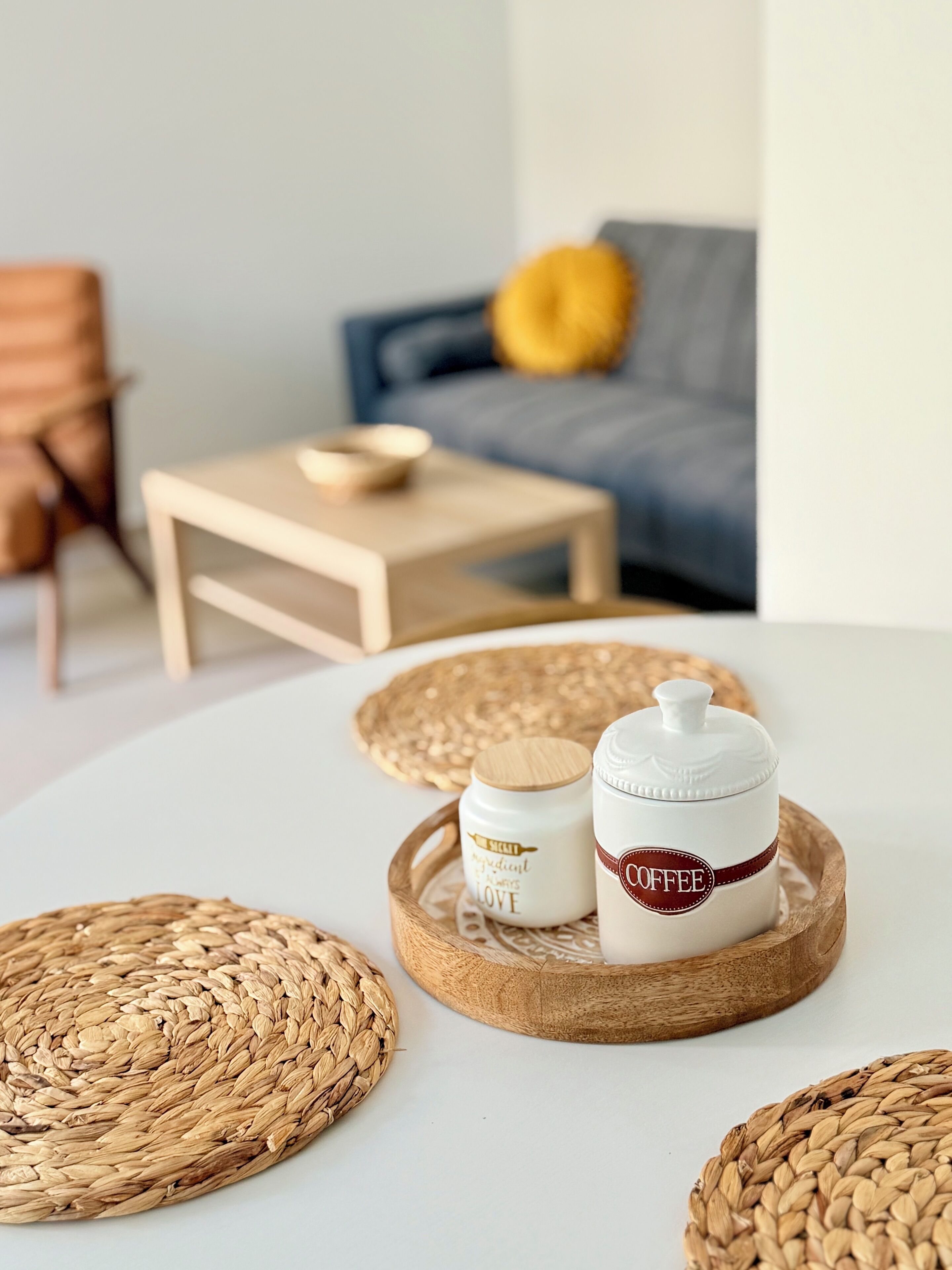 A cozy living room with a sofa, a small wooden table, and two woven placemats on a white table.