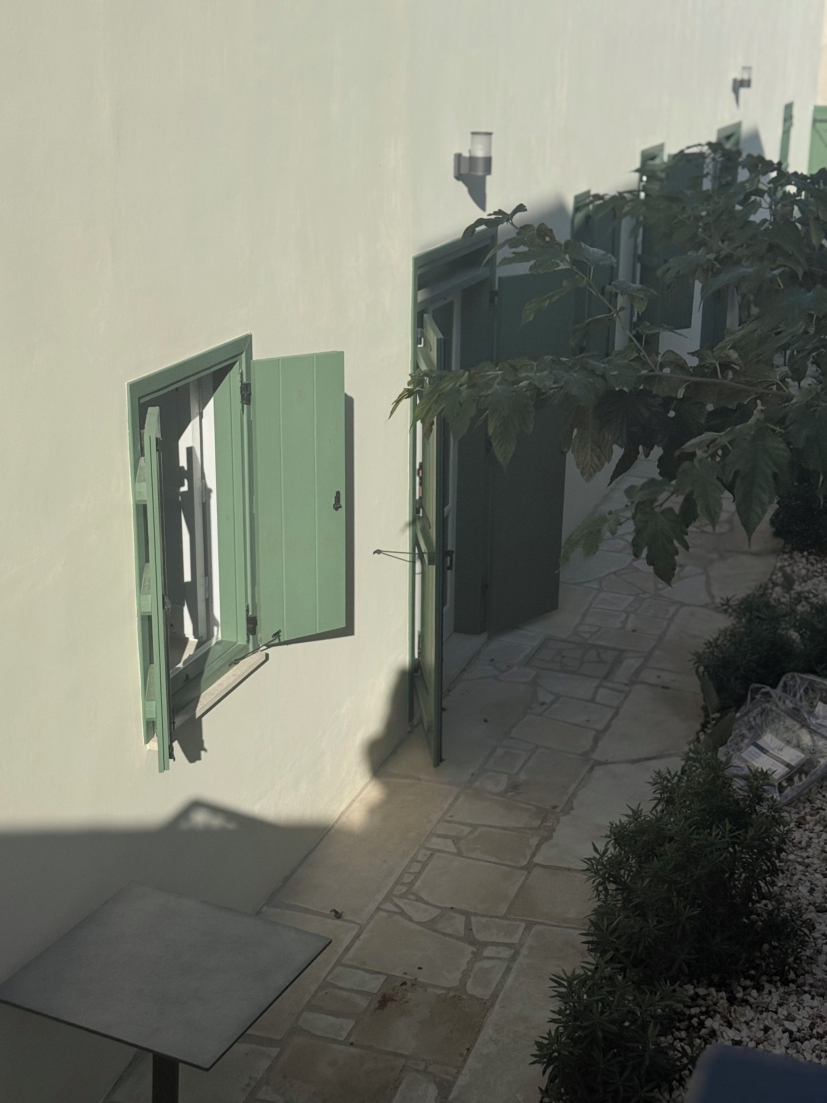 Un camí de pedra estret que condueix a un edifici amb persianes verdes i una taula petita.