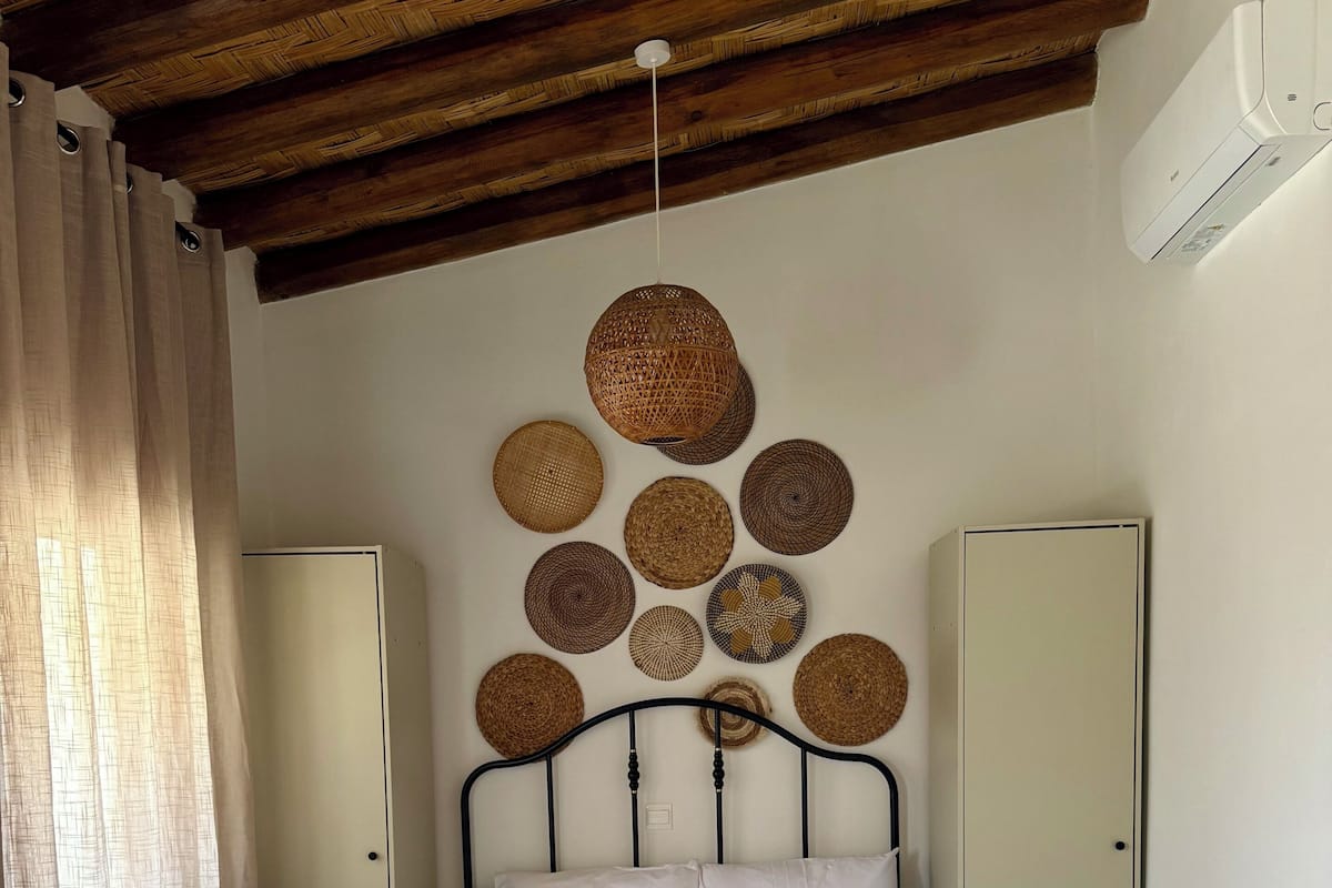 A bedroom with a bed, a wardrobe, a wardrobe mirror, a ceiling fan, and a wall-mounted air conditioner.