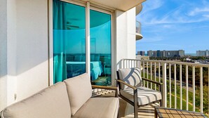 Ein Balkon mit einer Couch und einem Sessel, einer Schiebetür und Blick auf eine Stadtlandschaft.