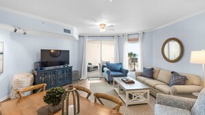 A living room with a television, sofa, coffee table, and dining table. - Lovely waterfront condo with balcony, pool, hot tub & pickleball (Santa Rosa Beach)