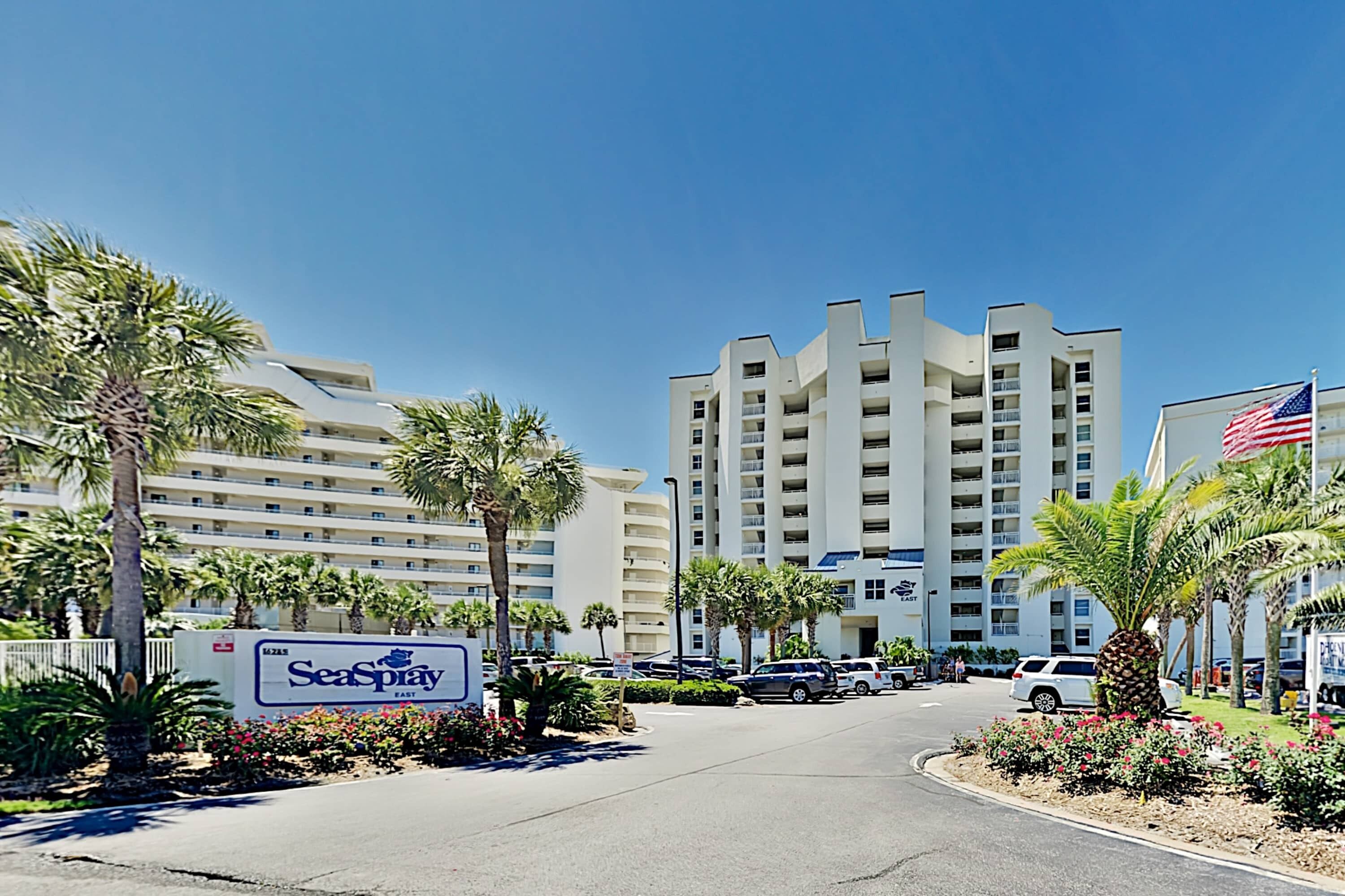 Ein Hotel mit modernem Design, ein gut sichtbares 'SeaSpray'-Schild, mehrere Stockwerke und ein Parkplatz mit Autos.