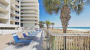 Ein Strandhotel mit mehreren Balkonen, einer Palme und einer Reihe blauer Liegestühle.