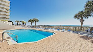 Ein Pool mit Liegestühlen und Palmen, mit Blick auf den Ozean.