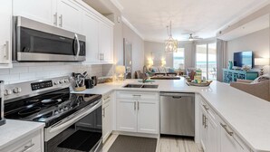 Una cucina moderna con mobili bianchi, piano cottura in acciaio inossidabile e forno a microonde. C'è un'area pranzo con vista sull'oceano.