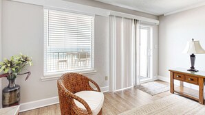 Ein Zimmer mit einem Korbstuhl, einem Schreibtisch mit Lampe, einer Pflanzvase und Blick durch ein Fenster mit Jalousien.